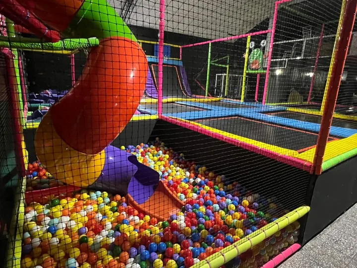 Resbaladilla tubular junto a trampolines y alberca multicolor de pelotas
